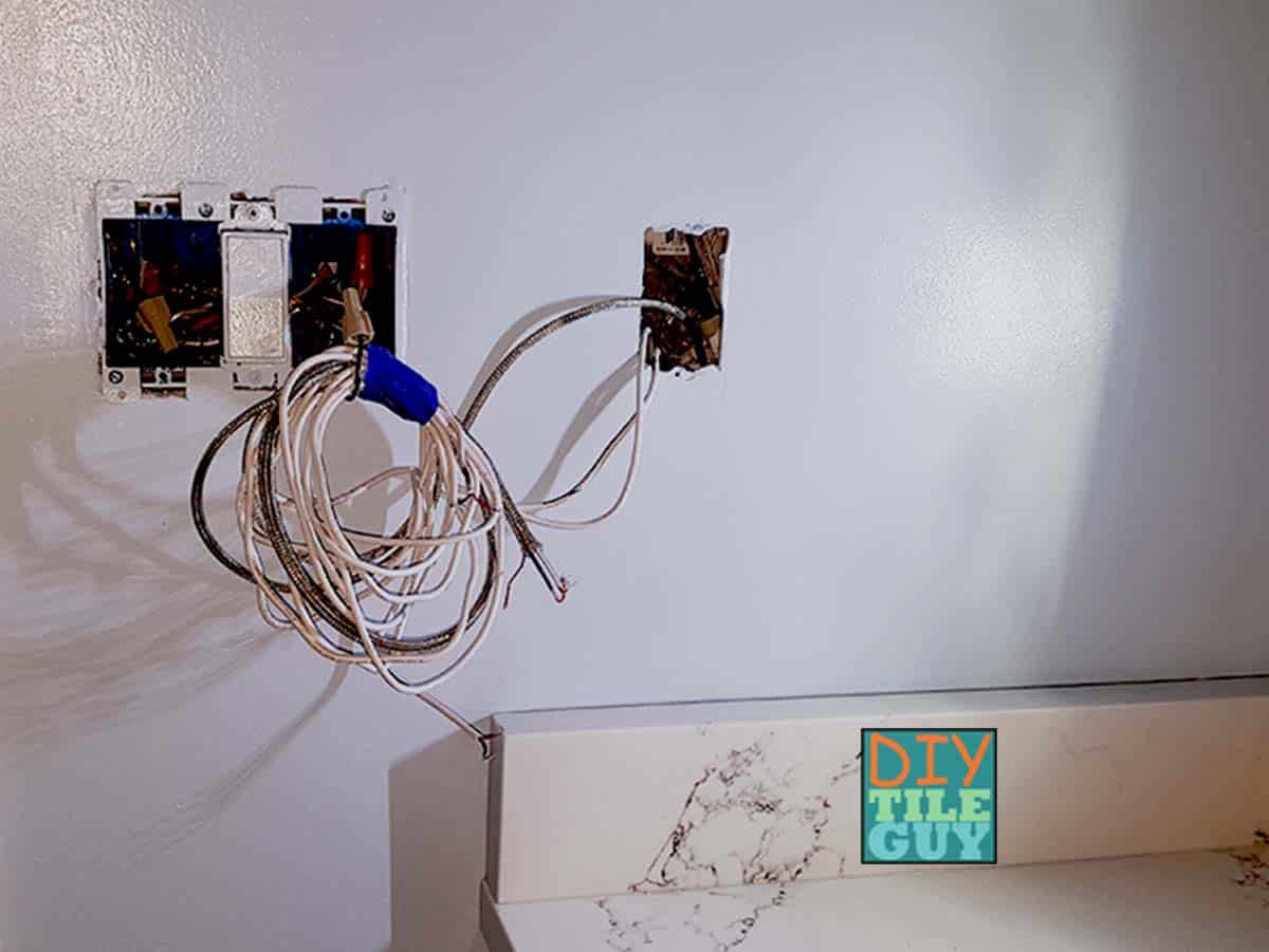 excess floor heat wires that haven't been trimmed yet are hanging out of the electrical rough in box on the wall