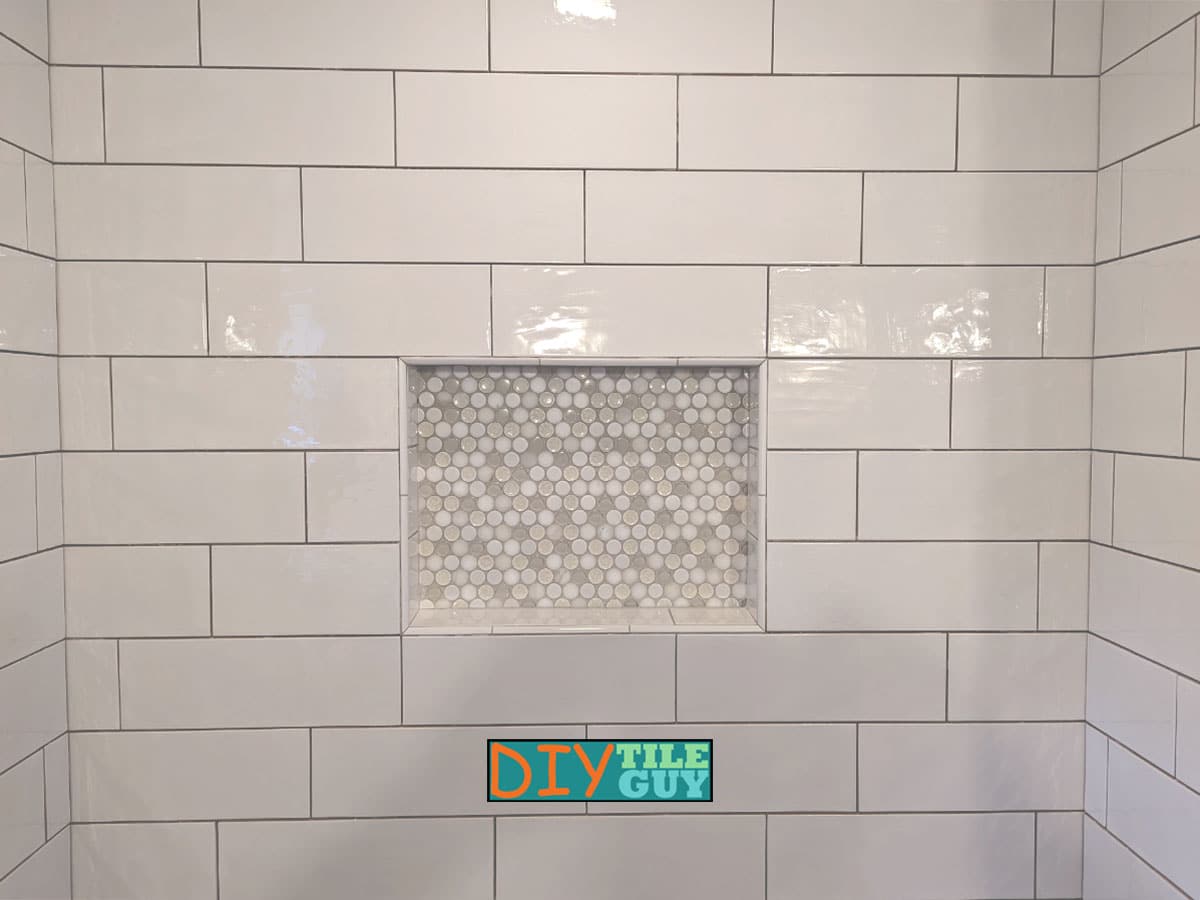 a centered shampoo niche that is incorporated into the layout of the large subway tile and has penny mosaics in the back