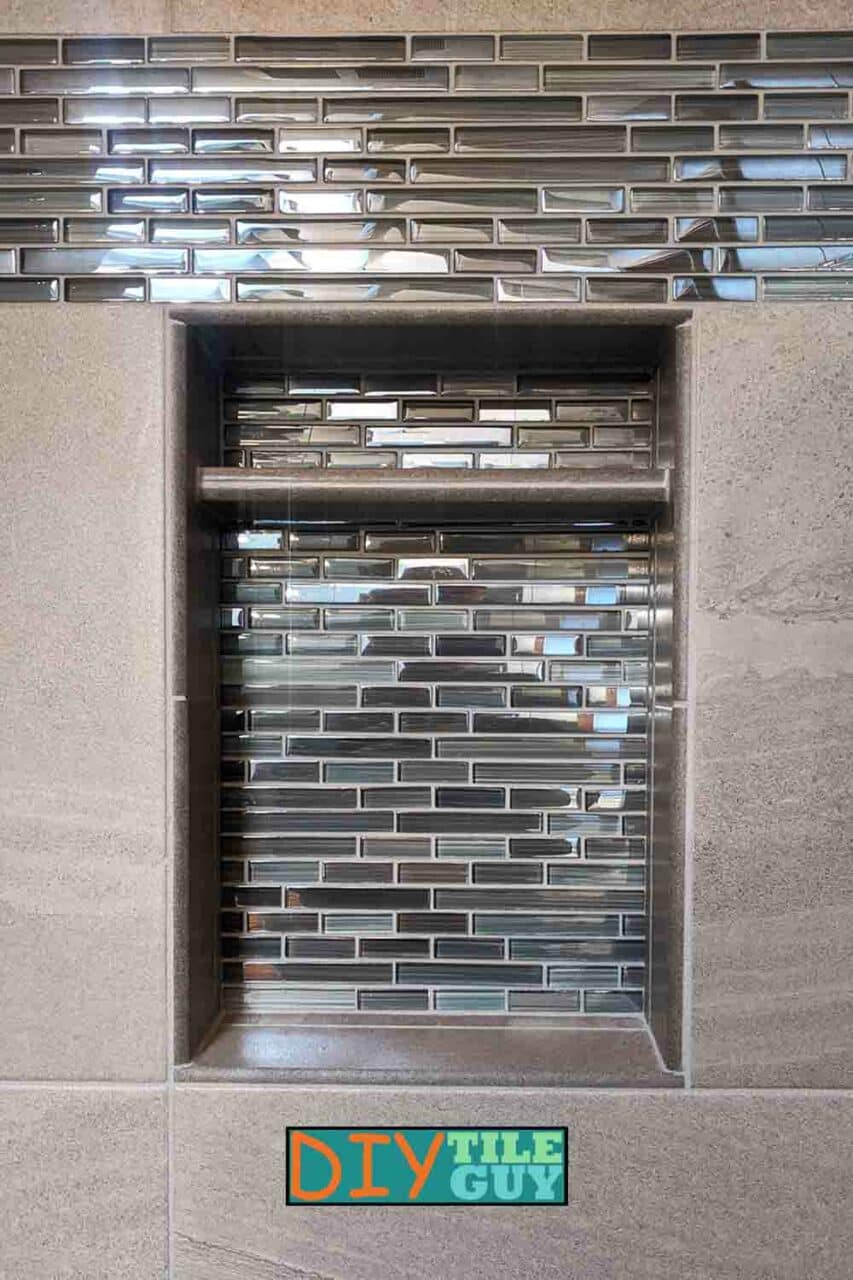 A recessed shower niche with bullnose tiles trimming all four sides with glass in the back.