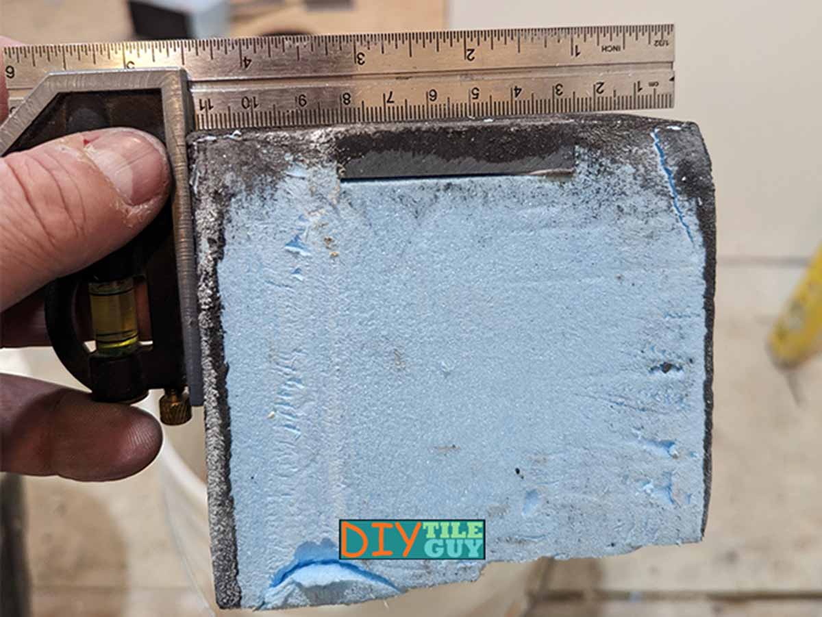 Looking at one end of the Wedi AT curb while holding a small square on top to check for pitch. This curb has reinforcement on the top to hold shower glass anchors.